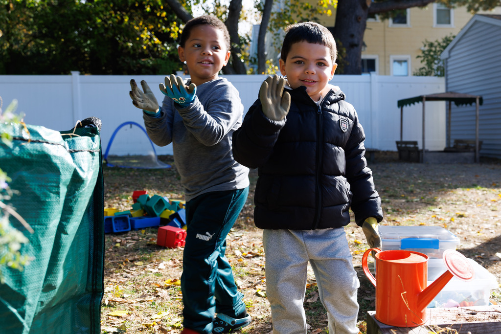 A student waves while another stands behind and smiles.
