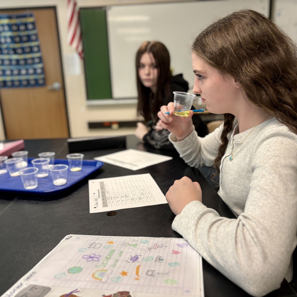 A student examines a small cup of yellow liquid during a science class.