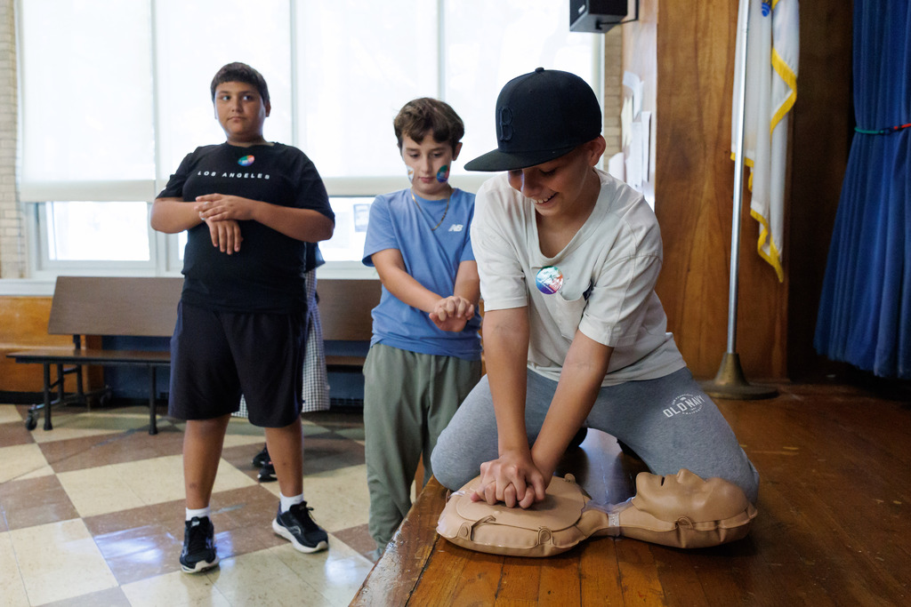 A student practices CPR while two others watch.