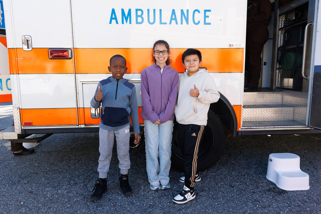 Three students smile outside of an ambulance.