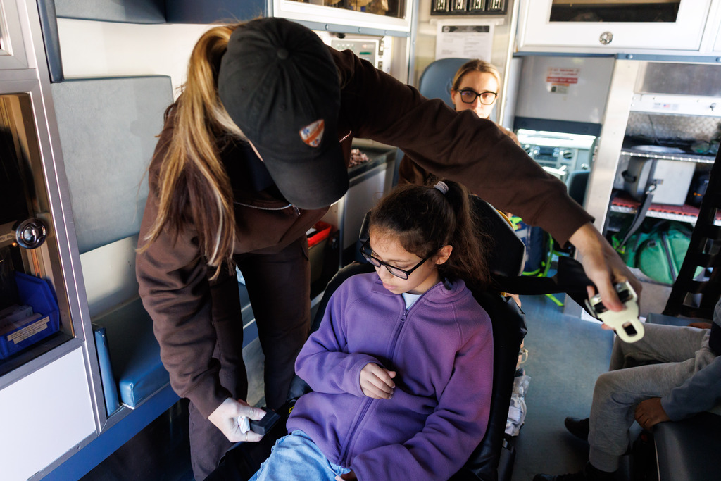 An EMS worker buckles a student into the gurney in the back of an ambulance.
