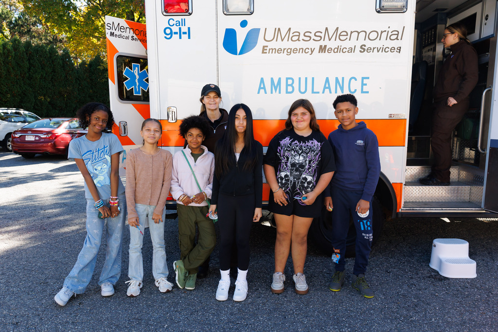 A group of students smile outside of an ambluance.