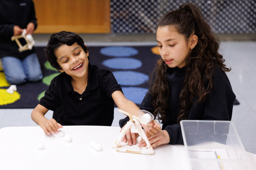 A student smiles while using a catapult to launch candy pumpkins.