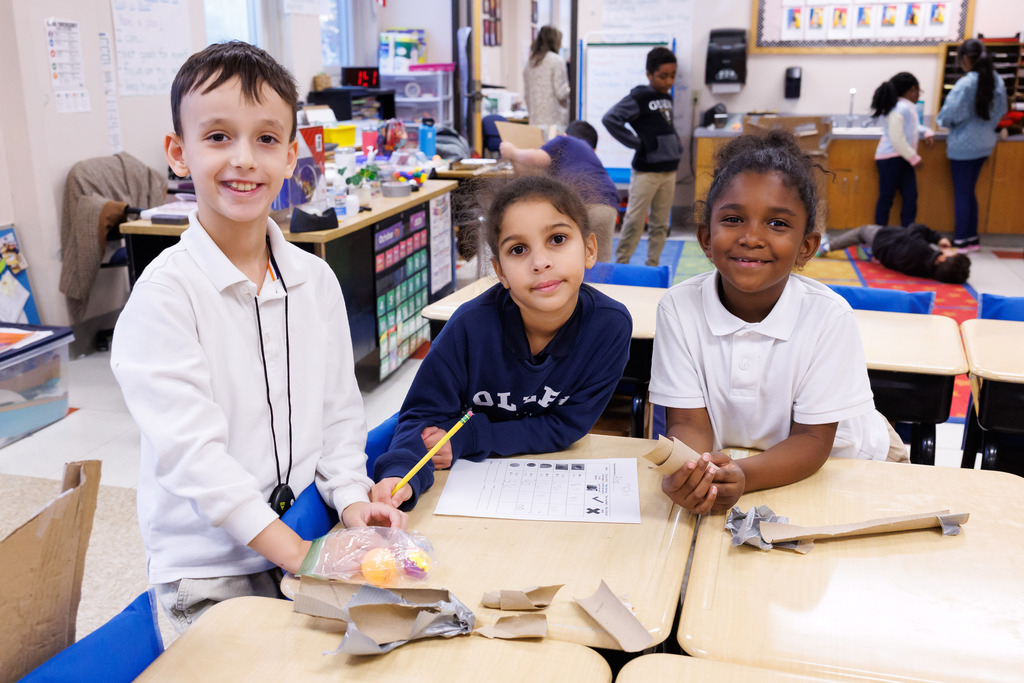 Three students smile for a photo while working on a science activity.