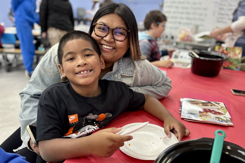 A smiling woman and a young boy pose closely together at a table covered with a red cloth.