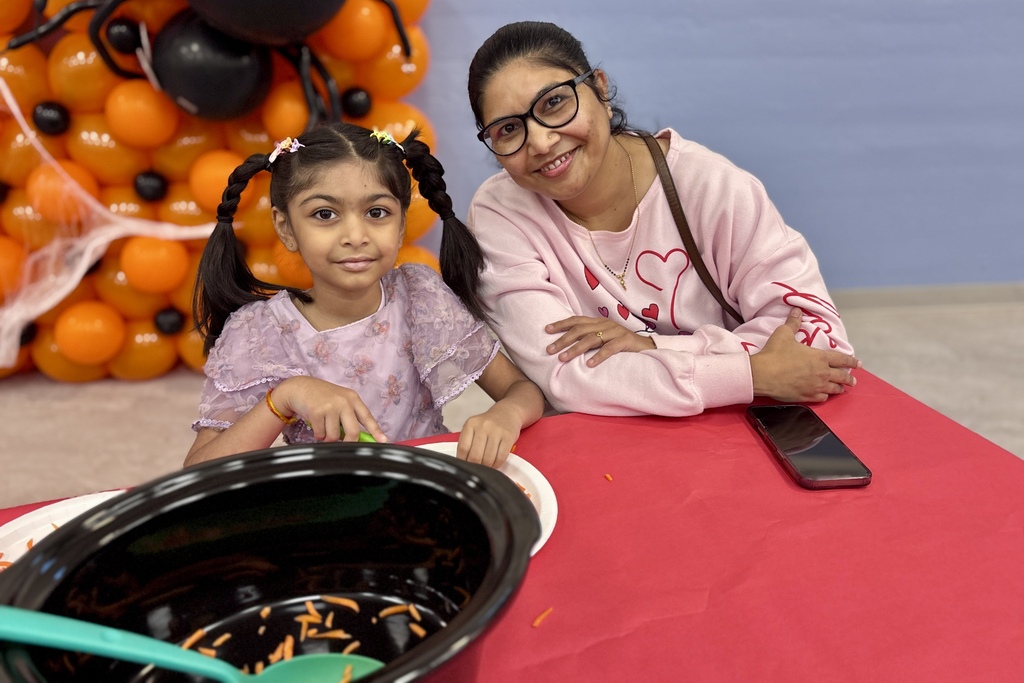 A smiling woman and young girl sit at a red table with a bowl of carrots.