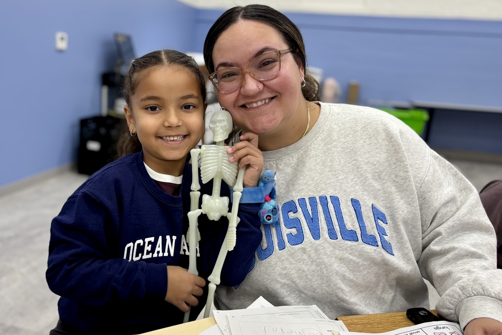 A smiling child and an adult woman pose together while holding a small plastic skeleton model.