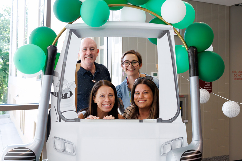 Four adults smile together for a photo in a golf cart themed photo booth.
