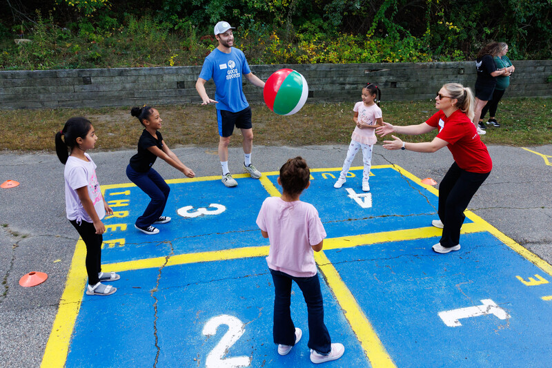 Students and adult volunteers volley a beachball while standing around in a circle.