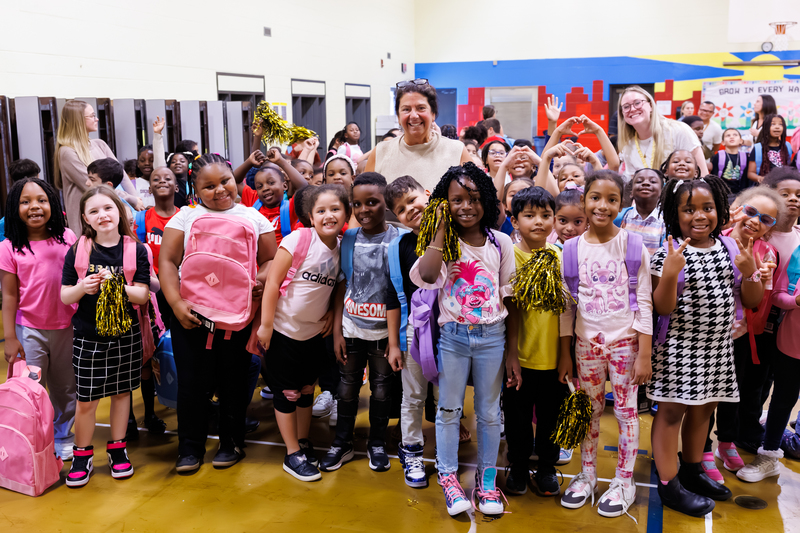 Chandler Elementary Community School teacher LuAnn Gallagher joins students as they smile following a backpack donation from New Orleans Saints cornerback and Worcester Public Schools alumnus Isaac Yiadom.
