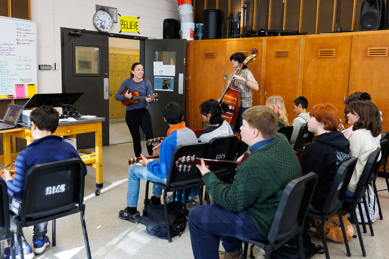 A teacher plays a ukulele in front of a class of students.