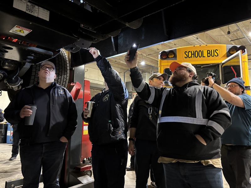 Workers underneath a bus inspecting it while it's lifted in a garage
