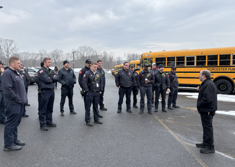 Firefighters stand outside a bus while an instructor speaks