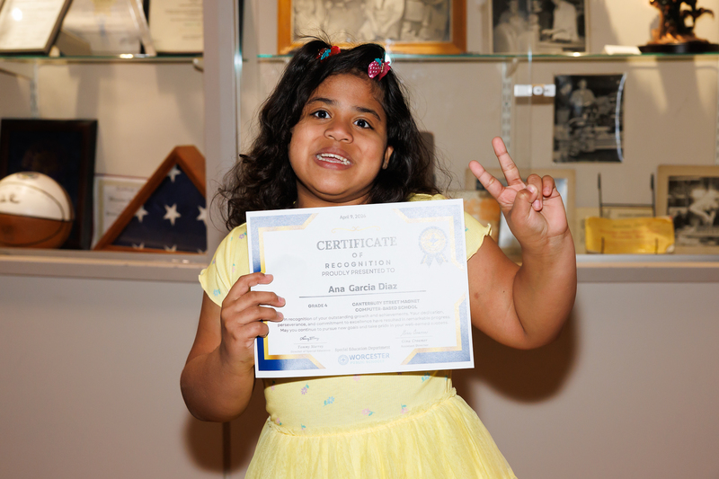 A young student gives a peace sign while holding up a certificate of recognition.