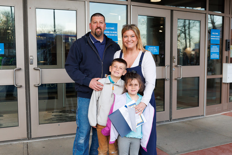 A family of four stand together outside for a photo.