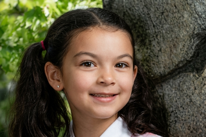 A young girl with dark hair in pigtails smiles warmly, wearing a white collared shirt.