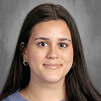 A young woman with long, dark hair smiles gently against a grey background.