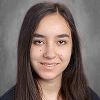 A young woman with long, dark hair smiles gently against a textured gray background.