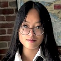 A young person with long dark hair and glasses looks directly at the camera.