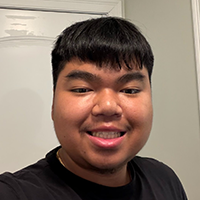 A young person with dark hair smiles at the camera, wearing a black t-shirt.
