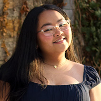 A young person smiles while standing in the snow next to a building covered in ivy.