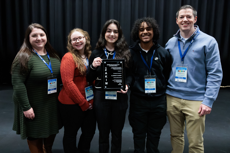 Five individuals, including two women and three young people, pose for a photo holding a plaque.