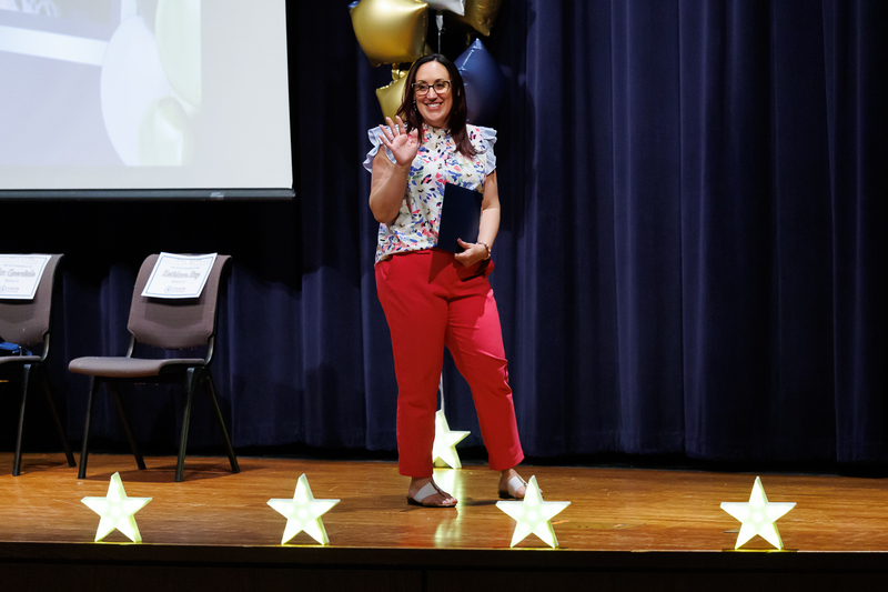 A teacher waves to the crowd while accepting an award on stage.