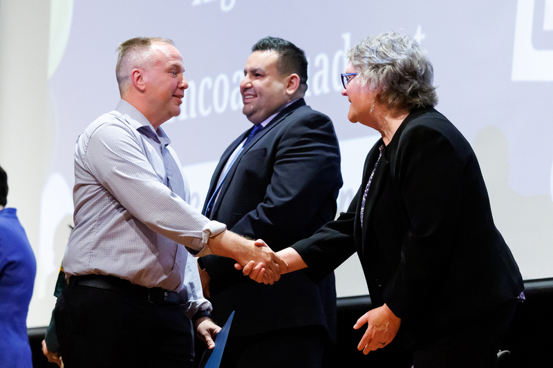 An adult shakes the hand of an elected official while walking on stage.
