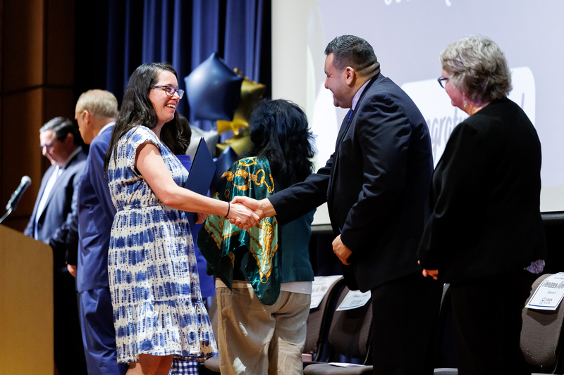 A woman shakes the hand of an elected official while walking across stage.