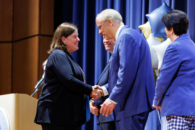 A woman shakes the hand of an elected official while walking across stage.