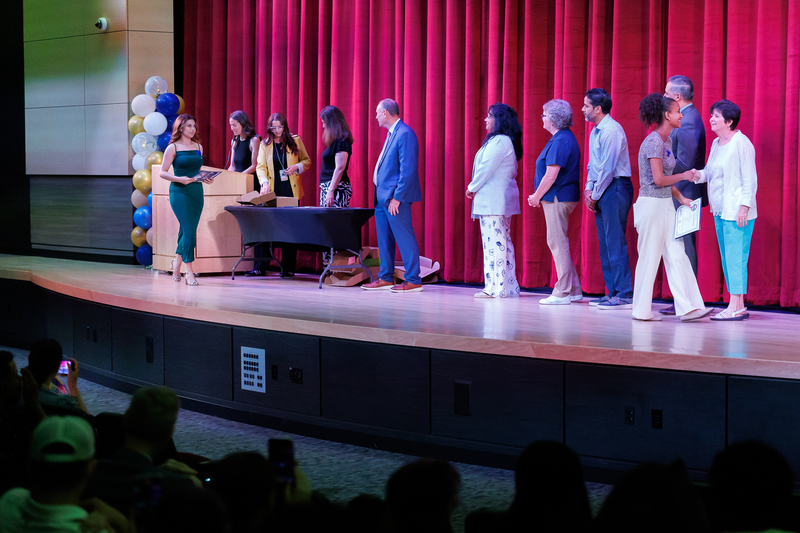 Students walk across stage during a celebration ceremony, shaking hands with elected officials.
