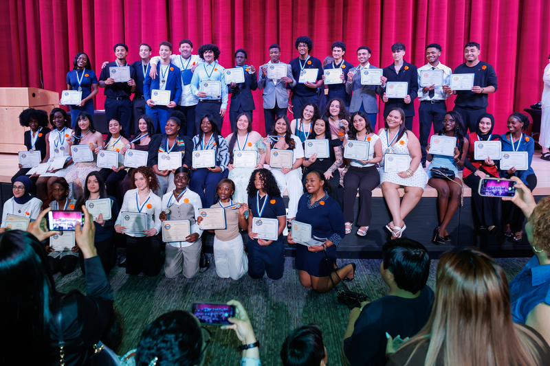A large group of students stand together on stage during a celebration ceremony.
