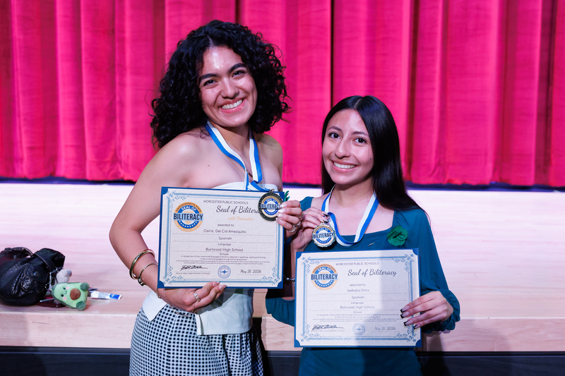 Two students stand together holding their certificates and medals following a celebration ceremony.