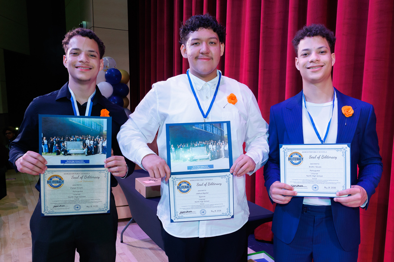 Three students stand together holding their certificates following a celebration event.