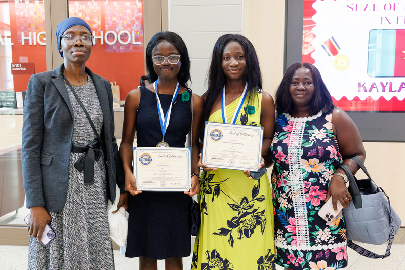 Two students and their parent stand together for a photo following a celebration ceremony.
