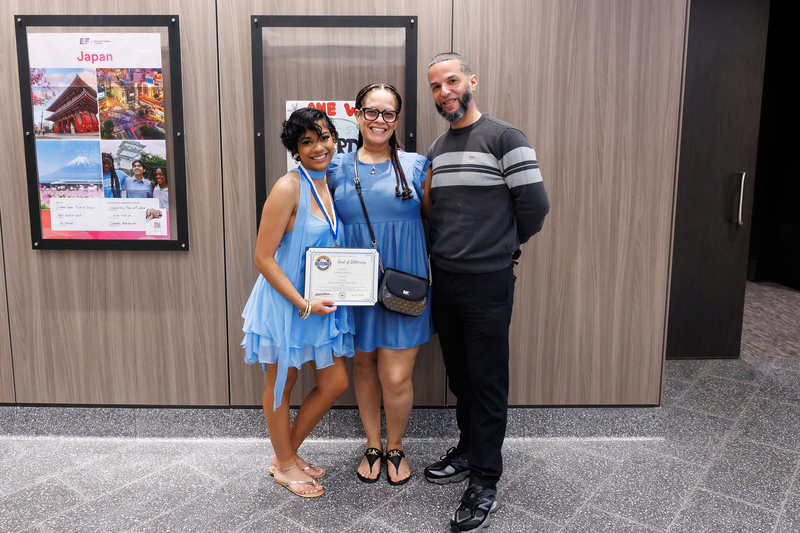 A student stands with their parents while holding up their certificate.