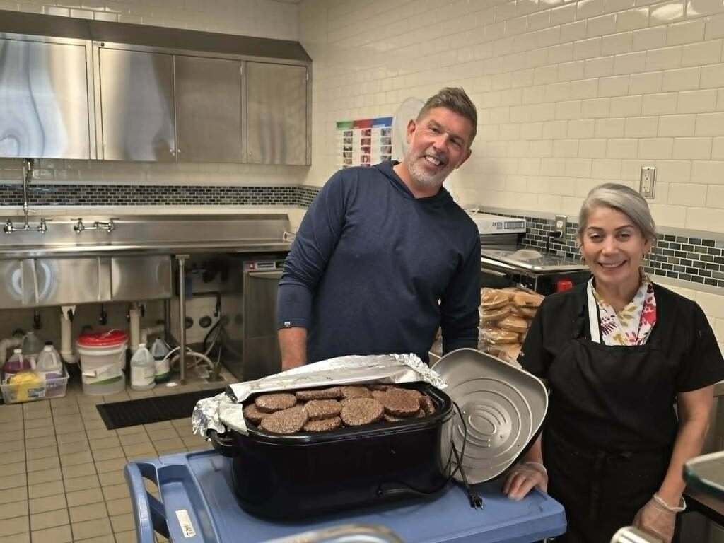 2 people standing in the Learning Center kitchen area with food to serve for lunch
