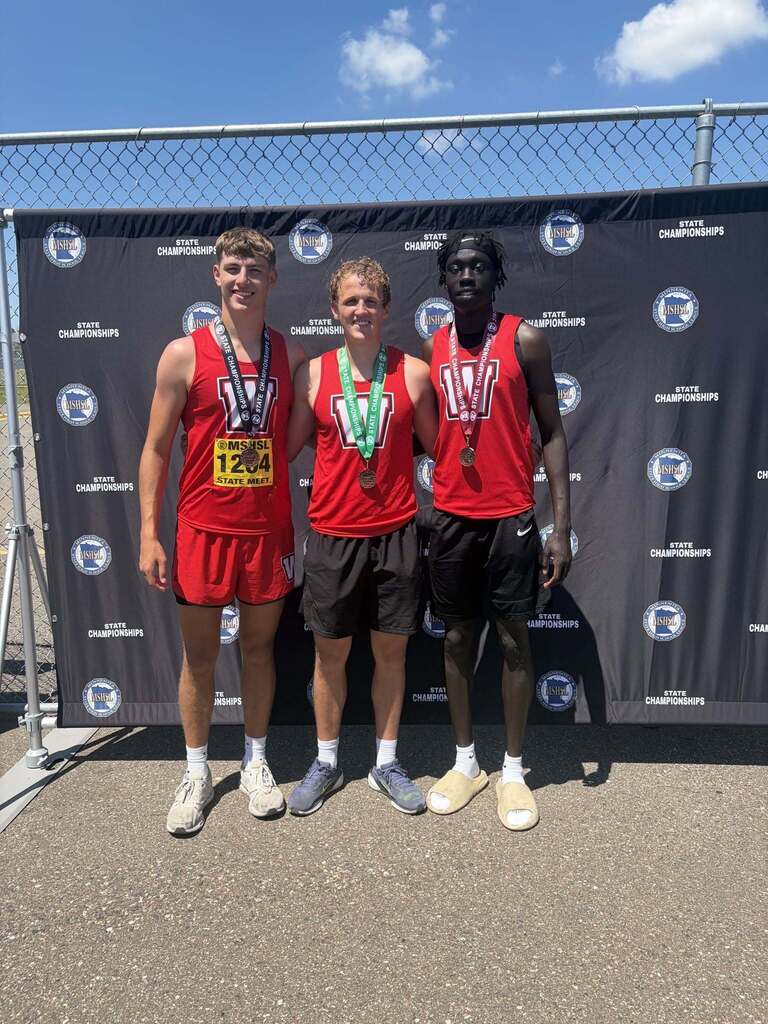 3 students standing in front of a backdrop at the track facility used for the MN State Track Meet 