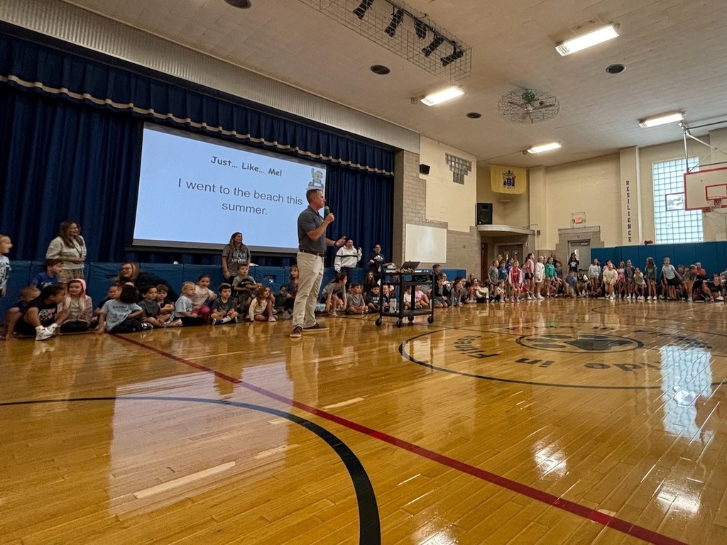 Students sitting in a circle in the gymnasium during school-wide morning meeting activity, "Just Like Me"