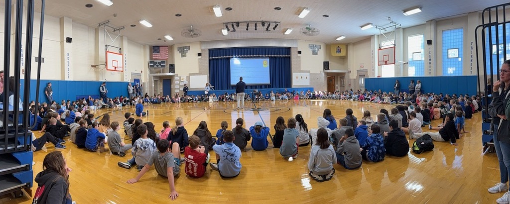 Students in gym gathered in a circle for school wide meeting.