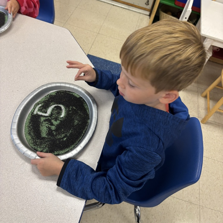 boy writing in a sand tray