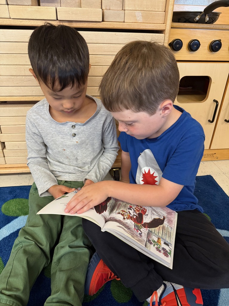Students partner reading a book while sitting on the classroom carpet.
