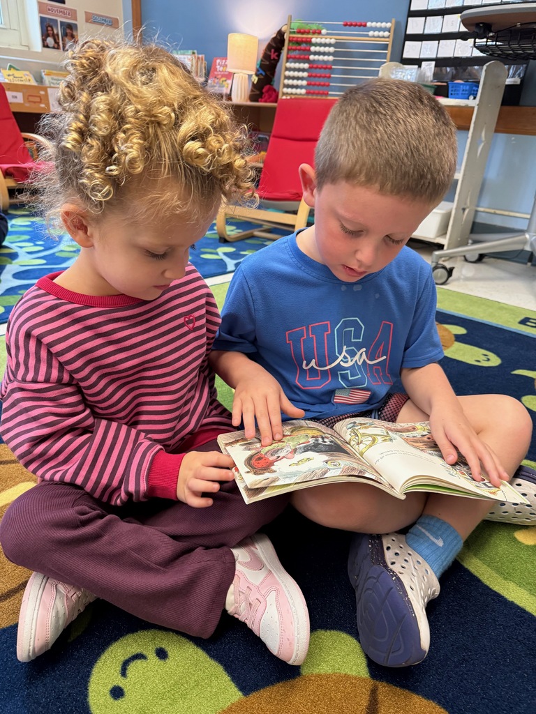 Students partner reading a book while sitting on the classroom carpet.