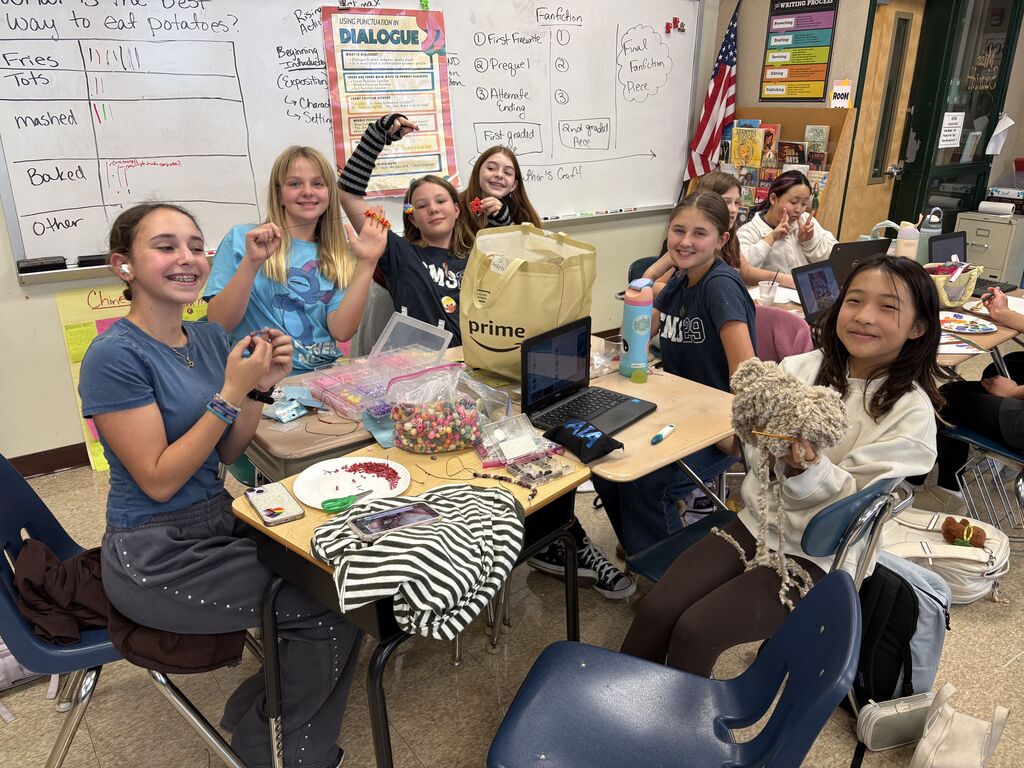A large group of students smile for a photo holding up a variety of handicrafts they are working on.