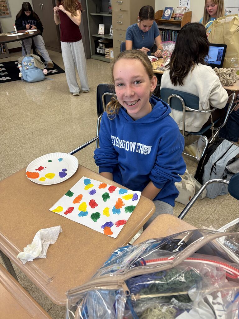 One student smiles with a paper plate of paint and an unfinished fingerpainting in front of her.