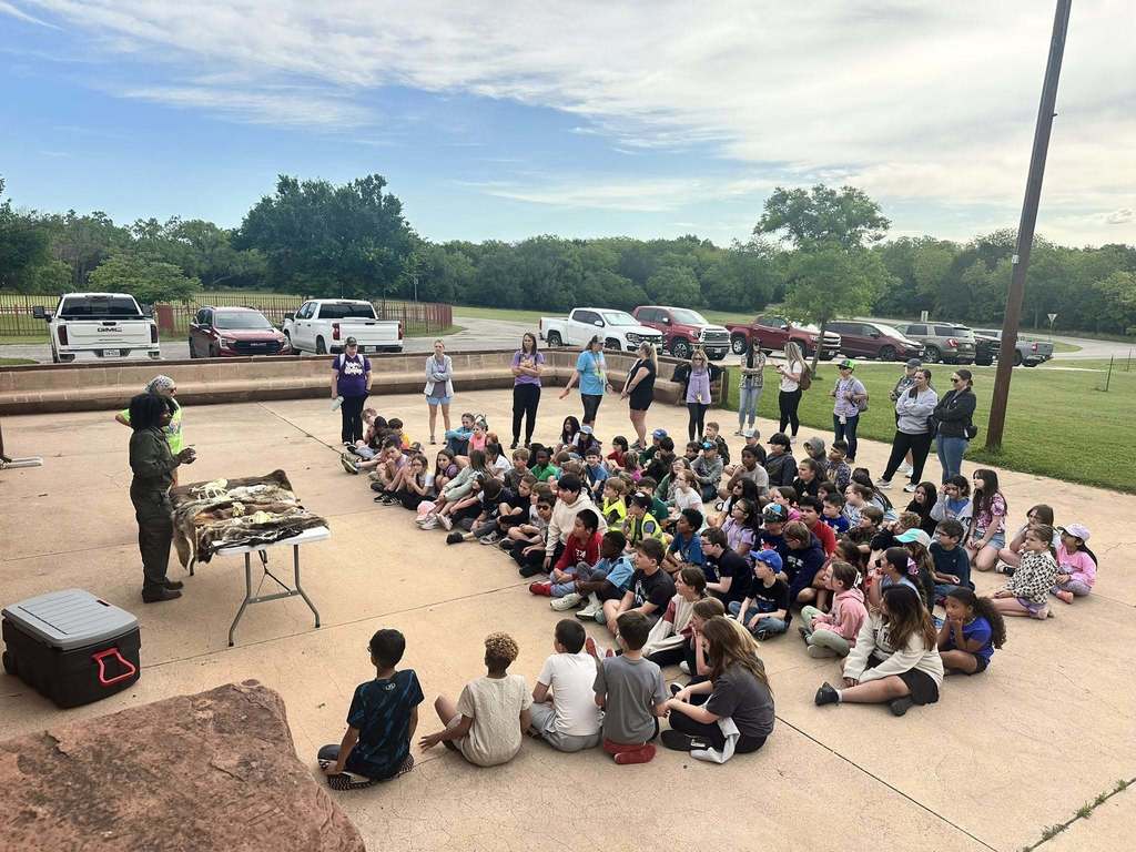 A wide group of students listen to a park ranger’s presentation featuring animal skulls and hides on display tables.