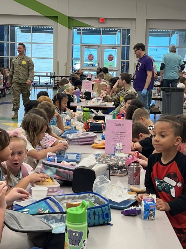 Military personnel eat lunch alongside students in a school cafeteria.