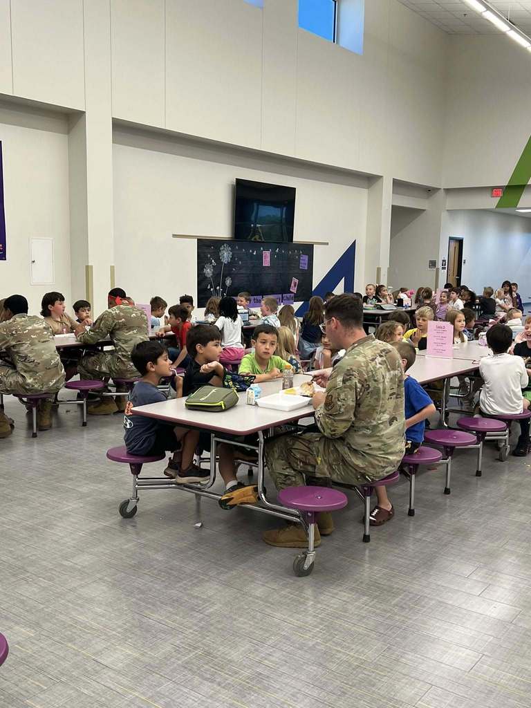 Military personnel eat lunch alongside students in a school cafeteria.