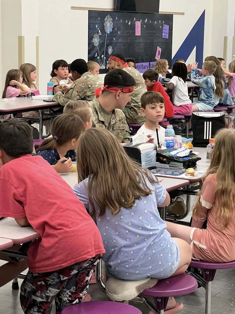 Military personnel eat lunch alongside students in a school cafeteria.