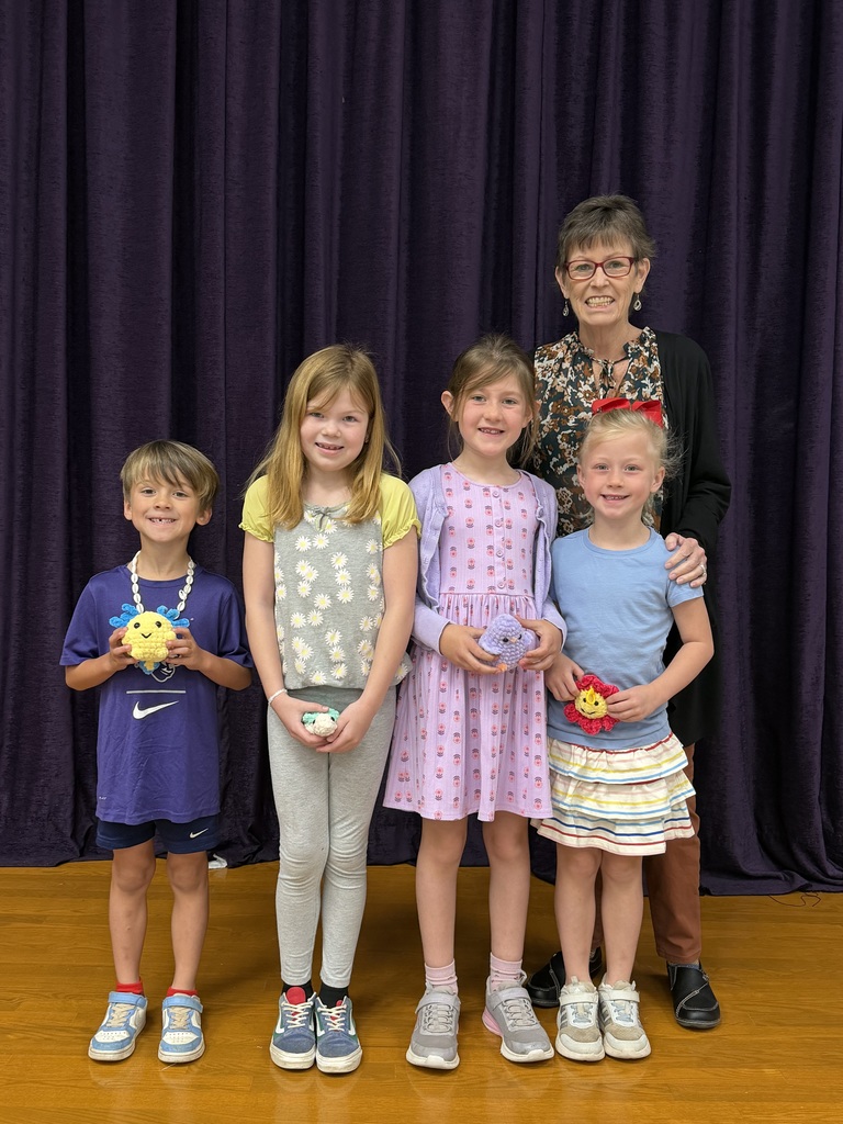 Four Wylie West Elementary students stand on stage with their librarian, smiling and holding handmade reading reward crafts.